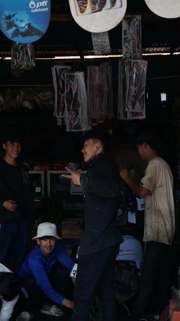 Young men laughing and joking in a dim motorbike shop hung with packaged decals in Luang Prabang, Laos