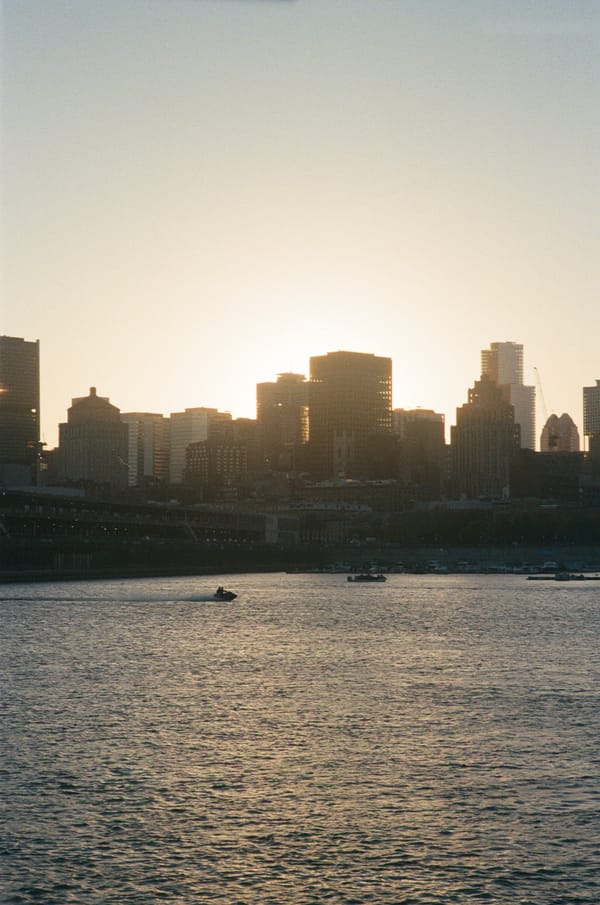 Downtown skyline silhouetted against a hazy sunset over the river, a jet ski crossing the water, in Montreal, Canada