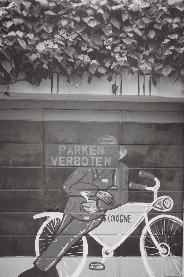 Black-and-white photo of a garage door mural of a man leaning on a bicycle under the words Parken Verboten