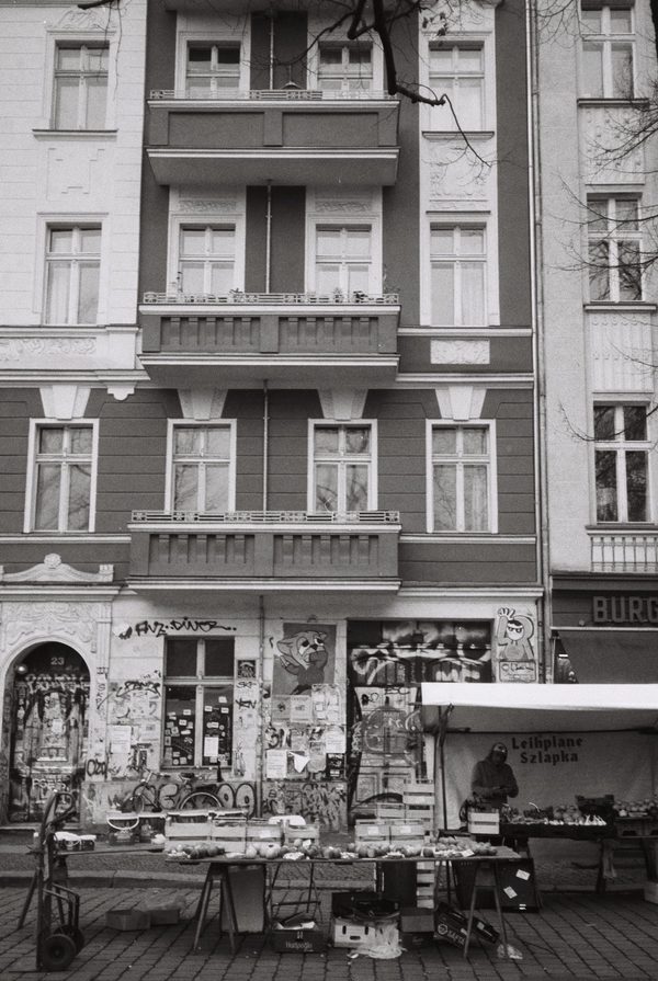 Black-and-white photo of an old apartment building with graffiti-covered ground floor and a market stall in front