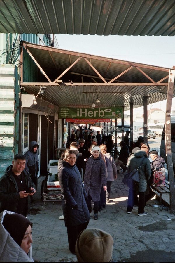 Shoppers in winter coats crowd a covered market passage lined with stalls on a bright cold day in Central Asia