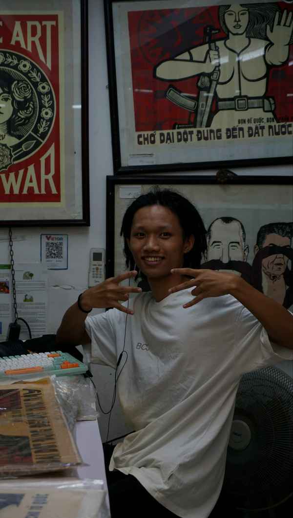 Young man flashing hand signs in a shop hung with vintage propaganda posters in Hanoi, Vietnam