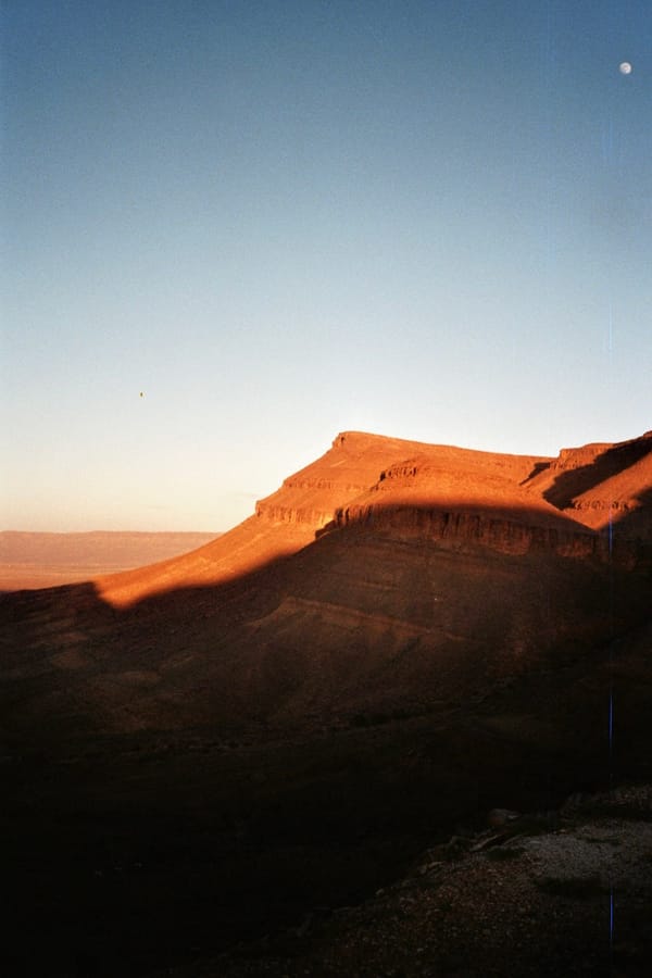 A flat-topped desert mesa glows orange in the last sunlight while the valley below falls into shadow, Morocco