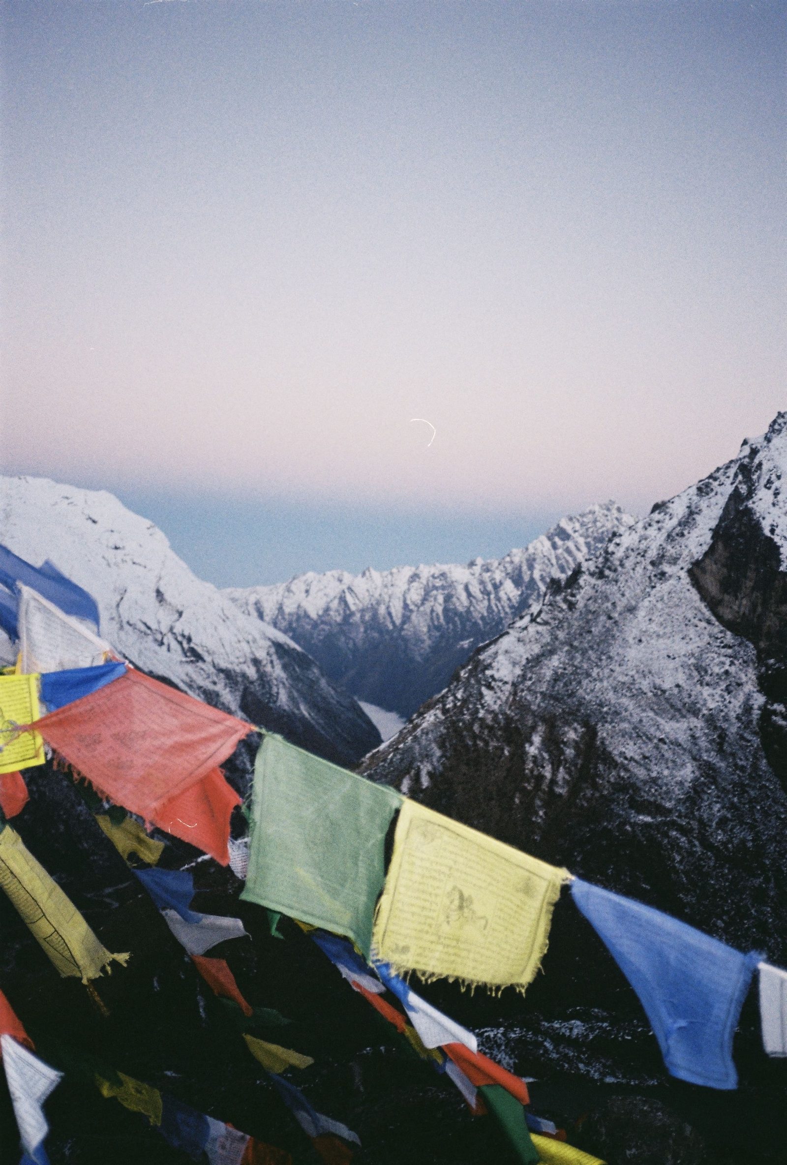 Colourful prayer flags in the foreground of snow-dusted peaks at dawn under a pale pink sky in Nepal