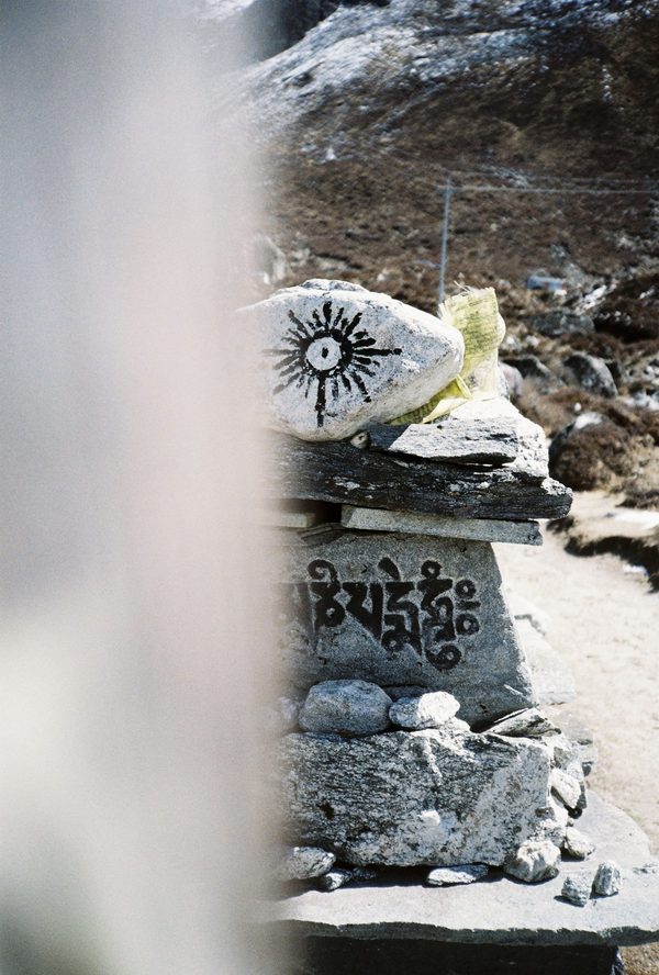 Stacked mani stones carved with Tibetan script and a painted sun symbol beside a mountain trail in Nepal