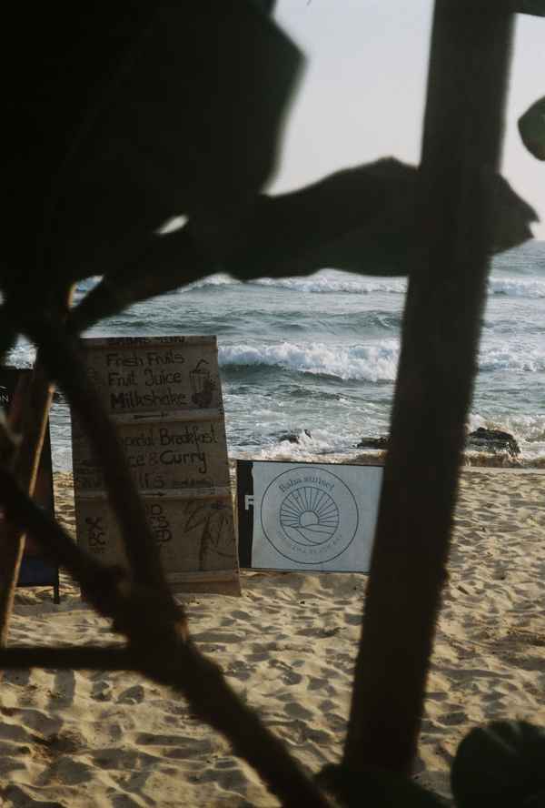 Handwritten menu boards for fruit juice and curry stand on the sand by crashing waves, seen through a beach hut in Sri Lanka