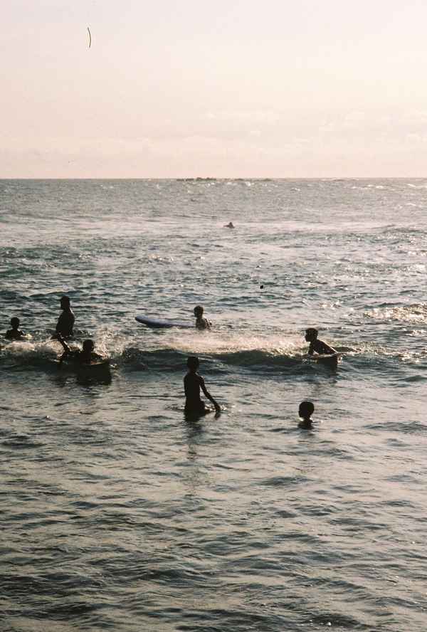 Children swim and play with bodyboards in the sea, silhouetted against glittering late-afternoon light in Sri Lanka